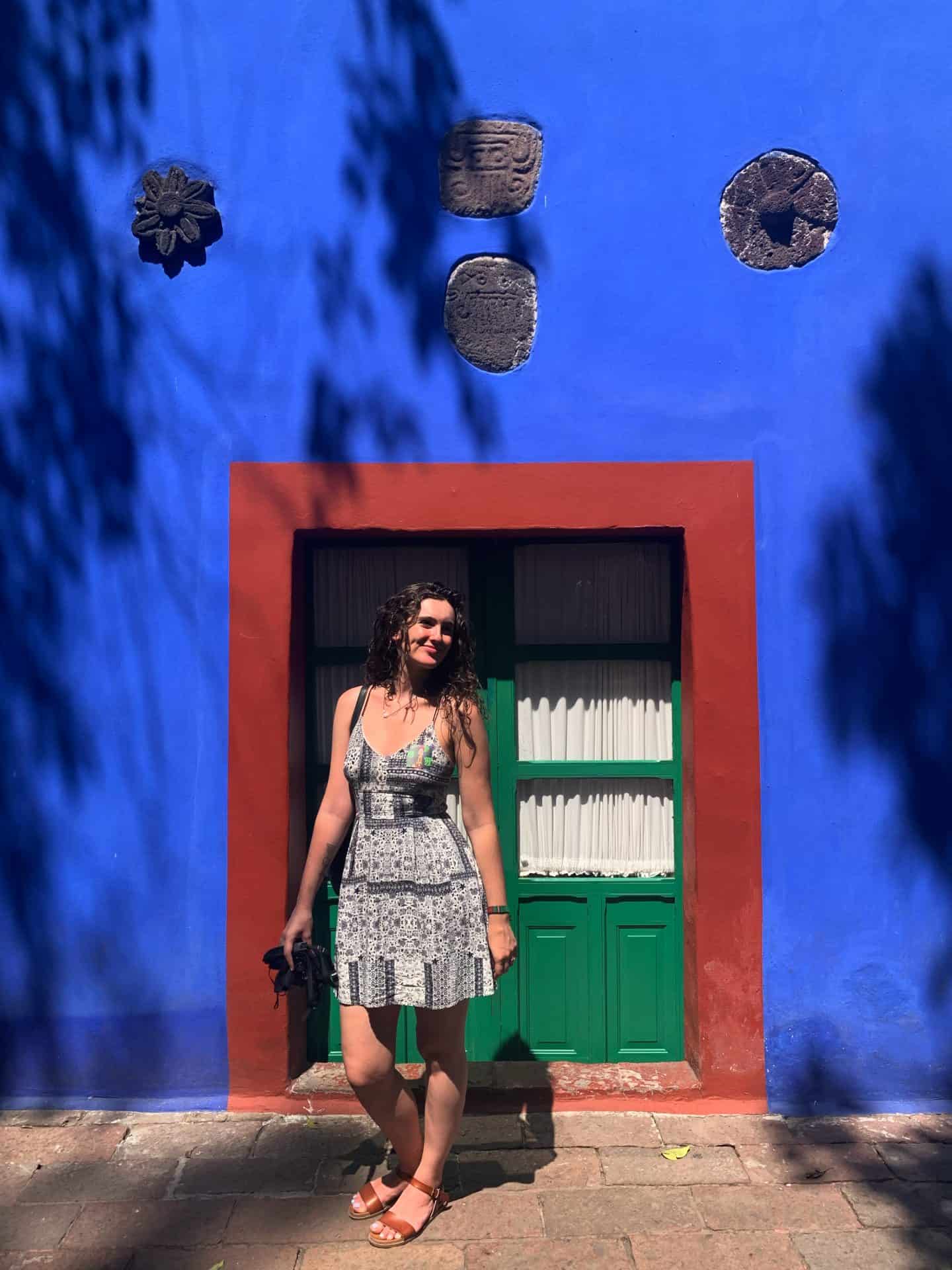 Woman stands in front of blue wall of Casa Azul, Frida Kahlo's house in Mexico City