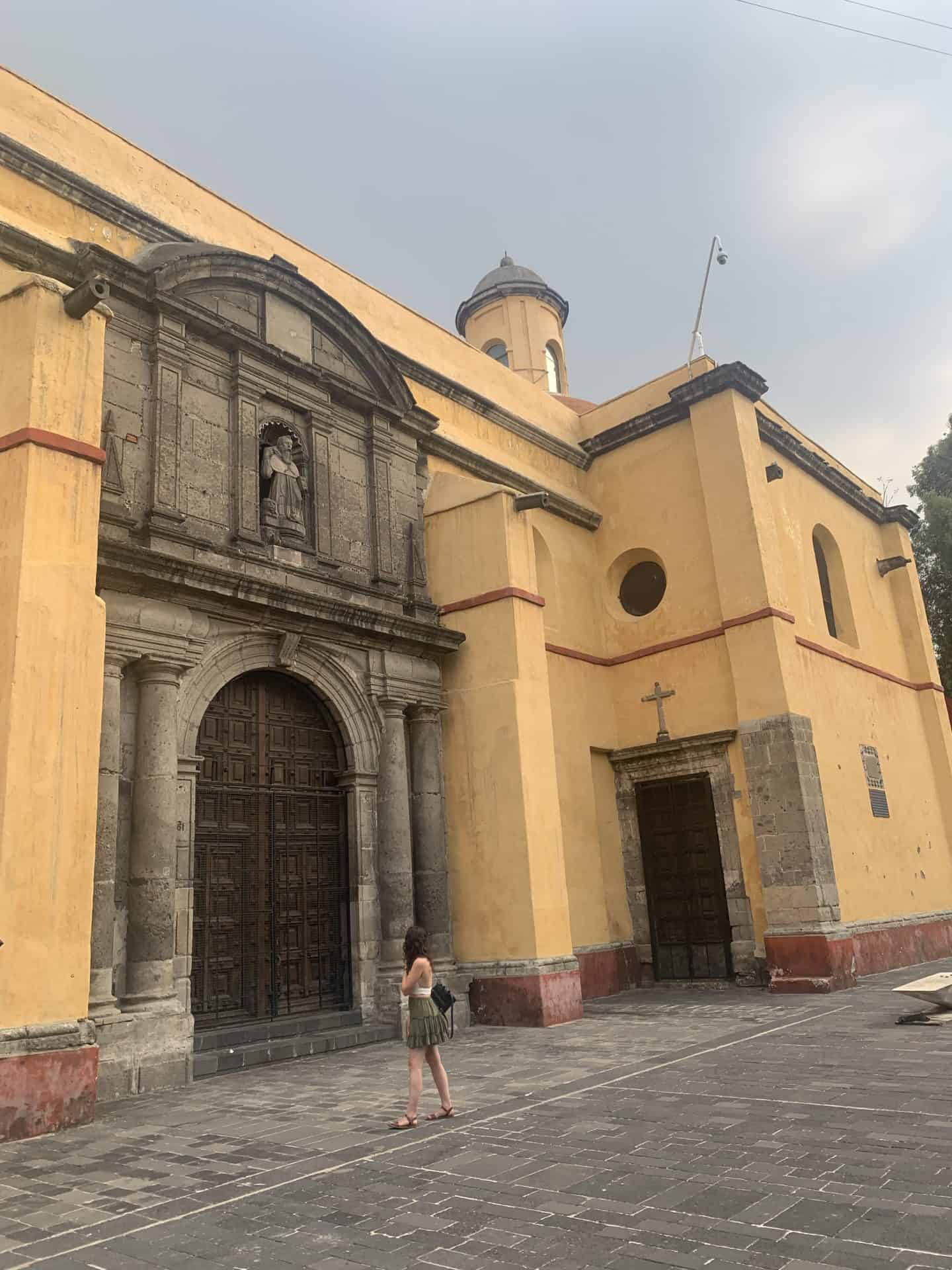 A woman walks in front of yellow church in Mexico City