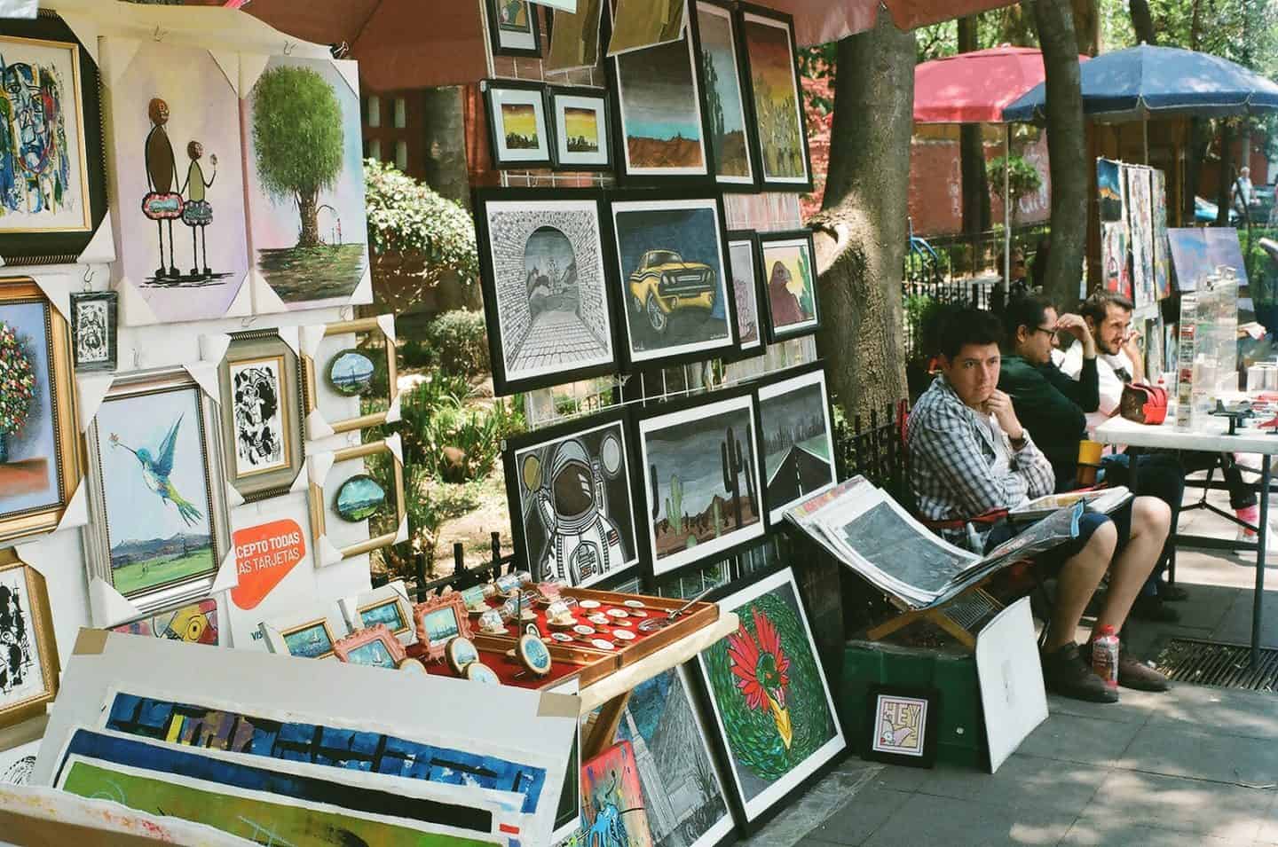 A wall of art in a park in Mexico City with artists seated next to the display.