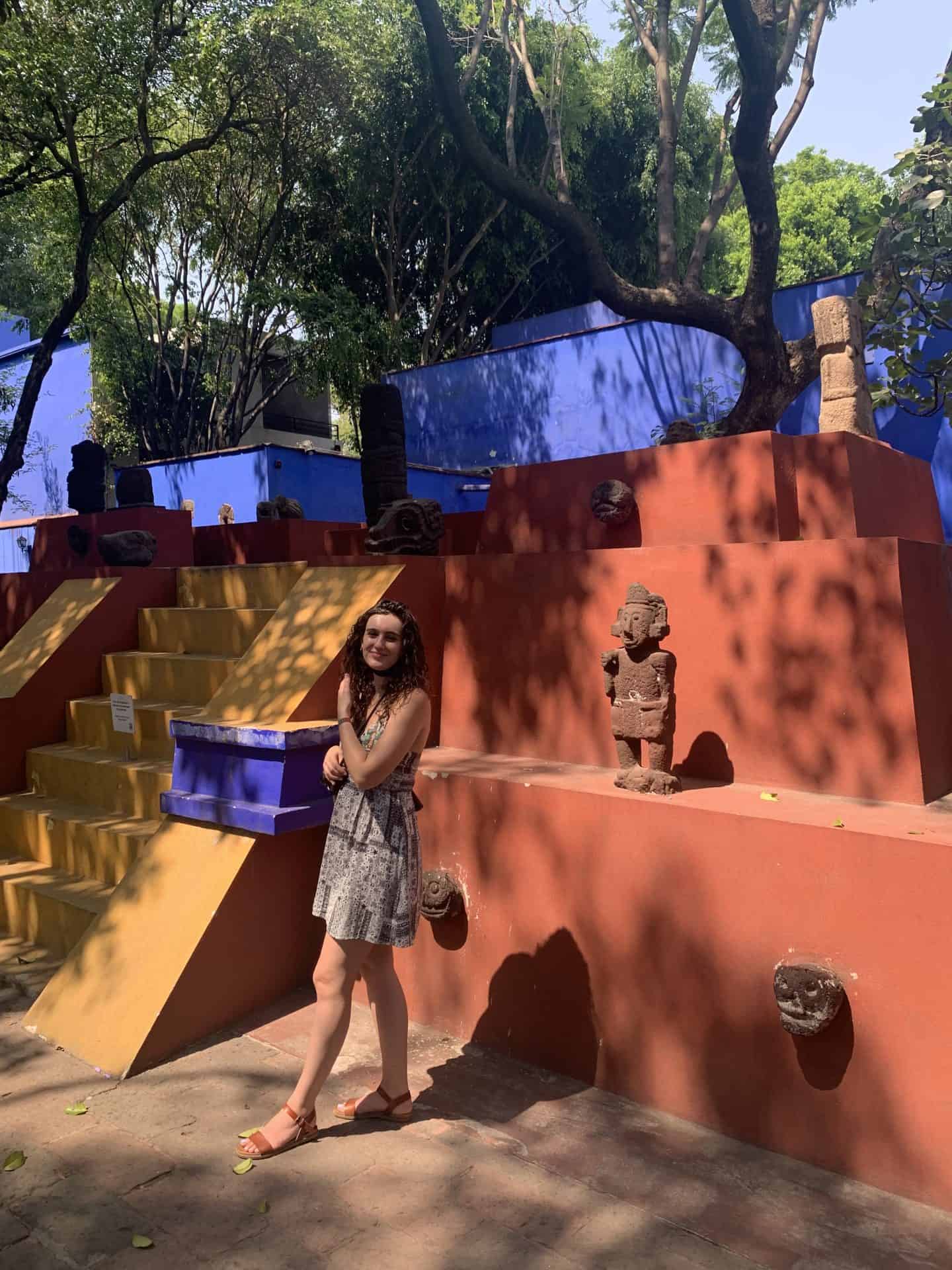 Girl standing in front of orange, yellow and blue pyramid in Casa Azul, Frida Kahlo's former home in Mexico City