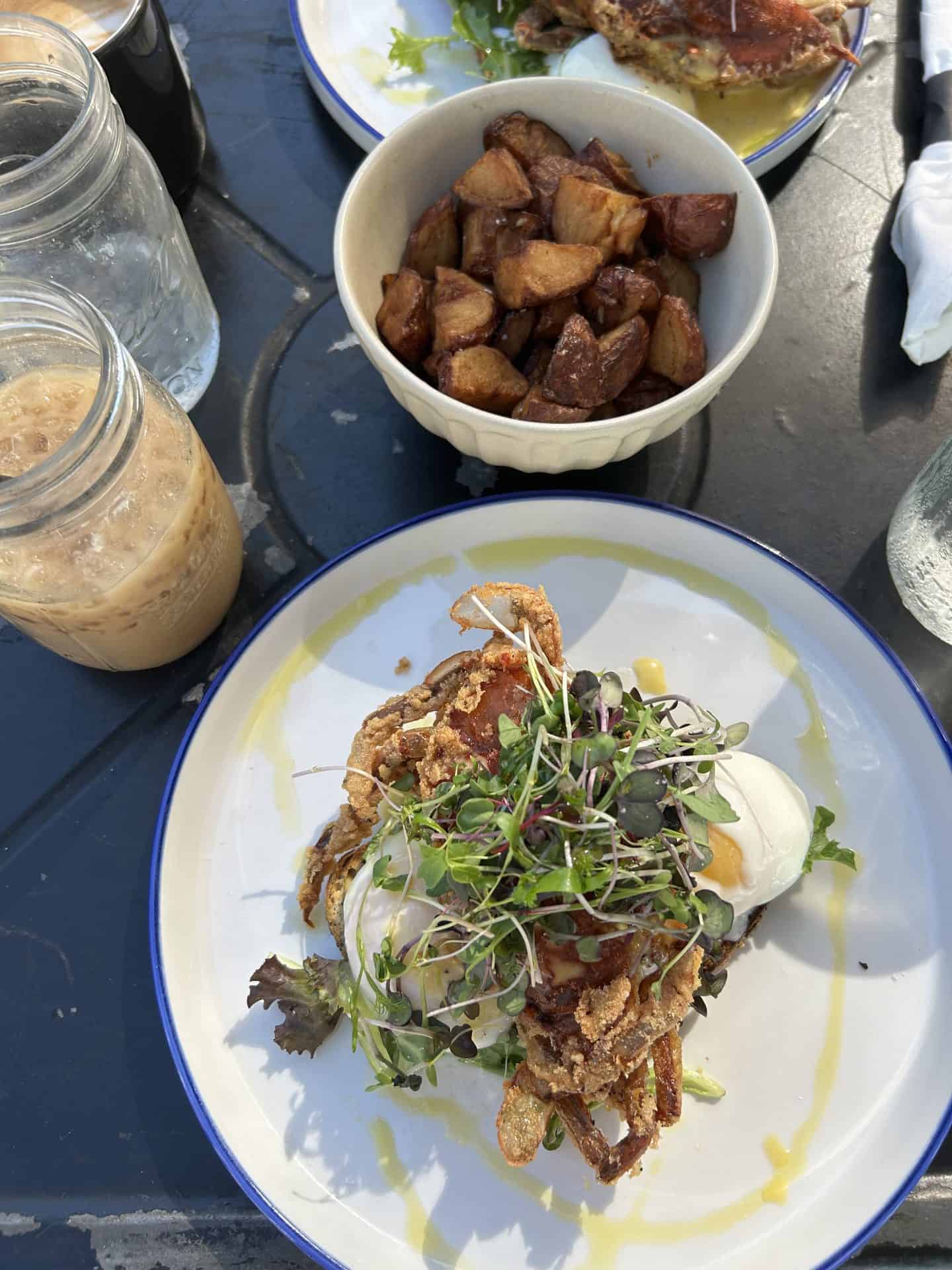 An egg dish with fried crab, a side of potatoes and iced coffee in New orleans.