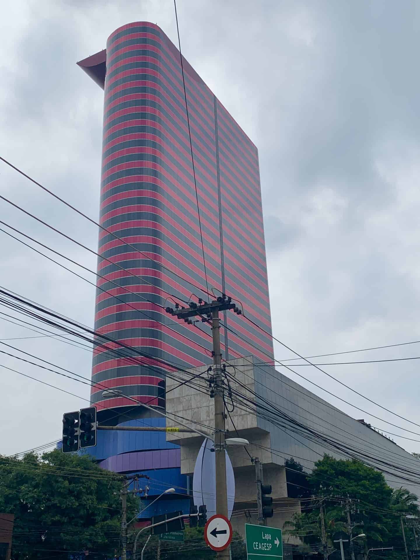 The Tomie Ohtake Institute building in São Paulo, Brazil. It is narrow with rounded sides, and red and black stripes on top, with blue and purple block-like layers on the bottom section,