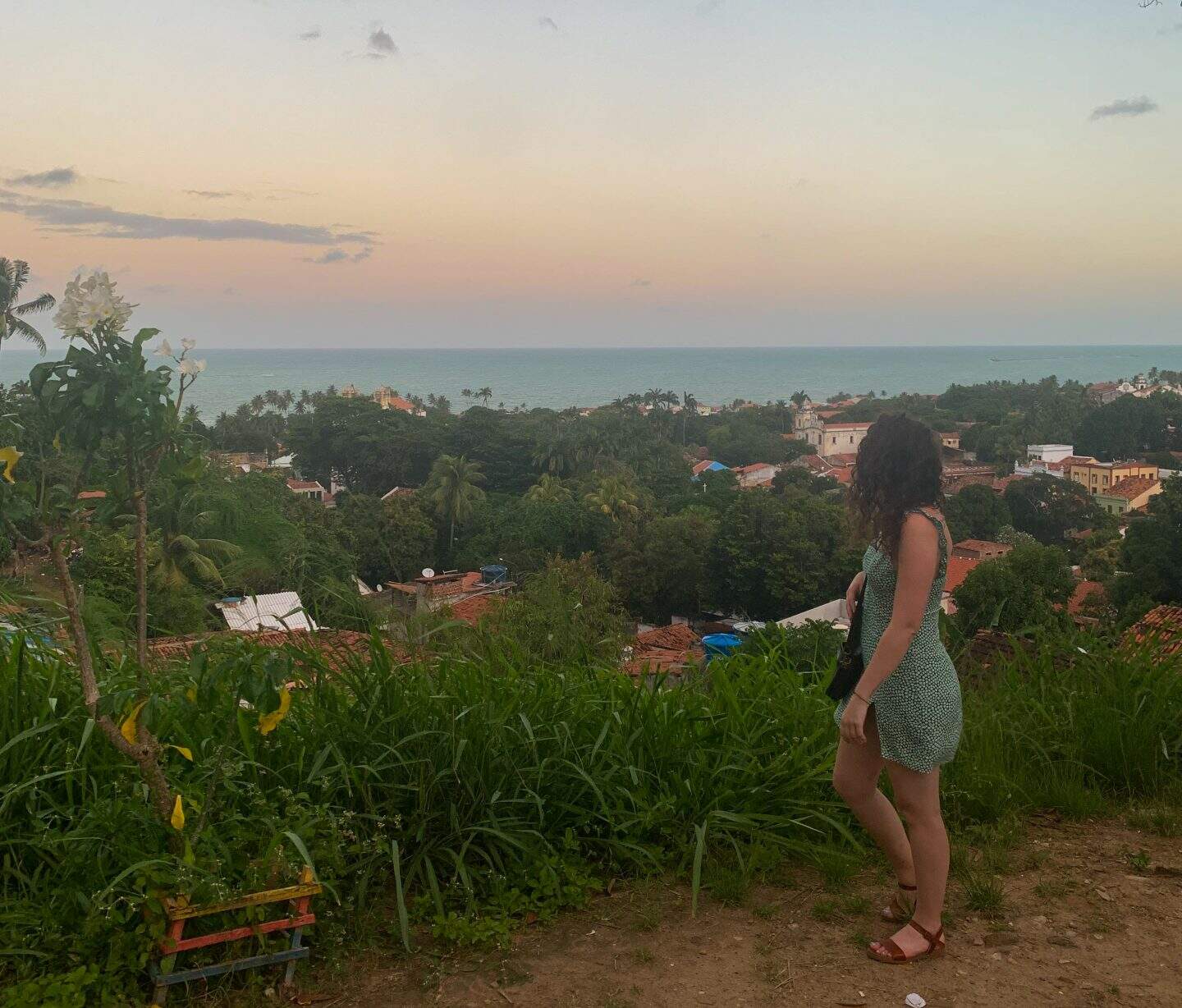 A woman in a green dress looks at the ocean behind her in Olinda, Brazil.
