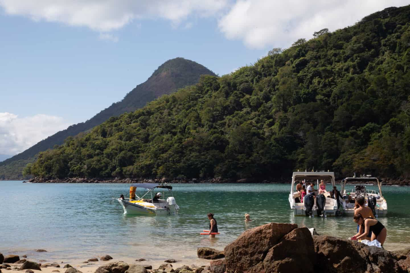 Green Lake, Ilha Grande, with a few small boats and people in the water. Trees and a mountain are behind the green water.