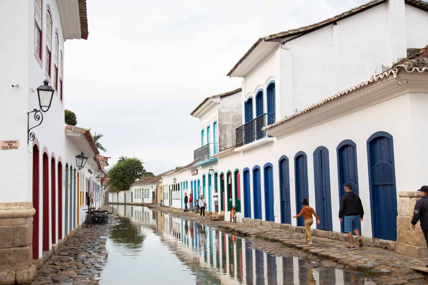 People walk along the sidewalk of a flooded street in Paraty, Brazil.