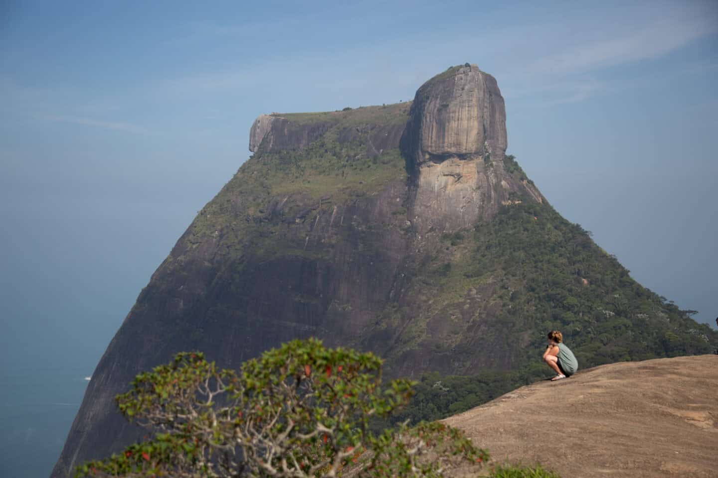 A person squats in front of a mountain in Pedra Bonita, a hike in Tijuca Forest, Rio de Janeiro.