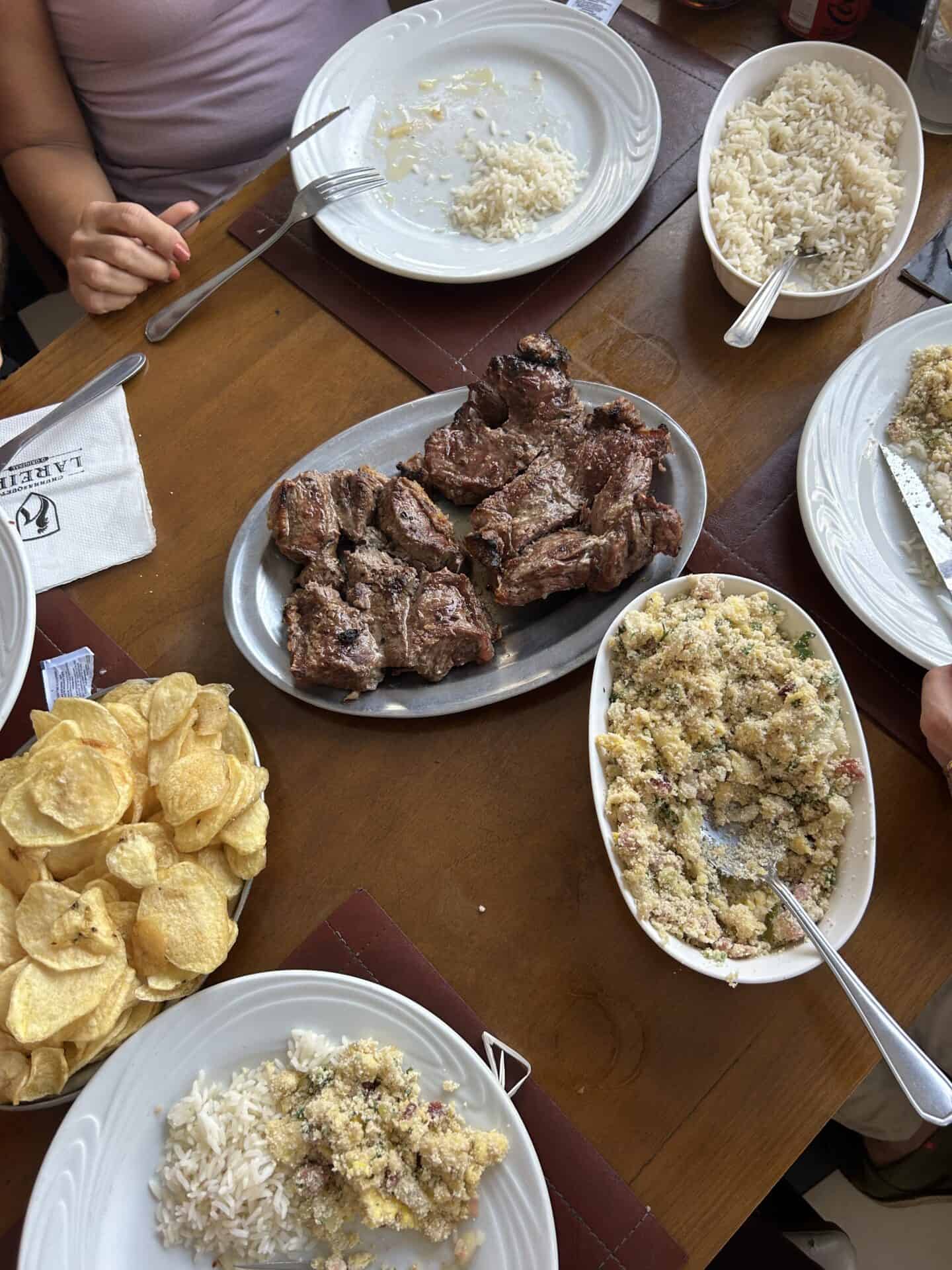 A table with steak, farofa, potato chips, and rice, in Rio de Janeiro.