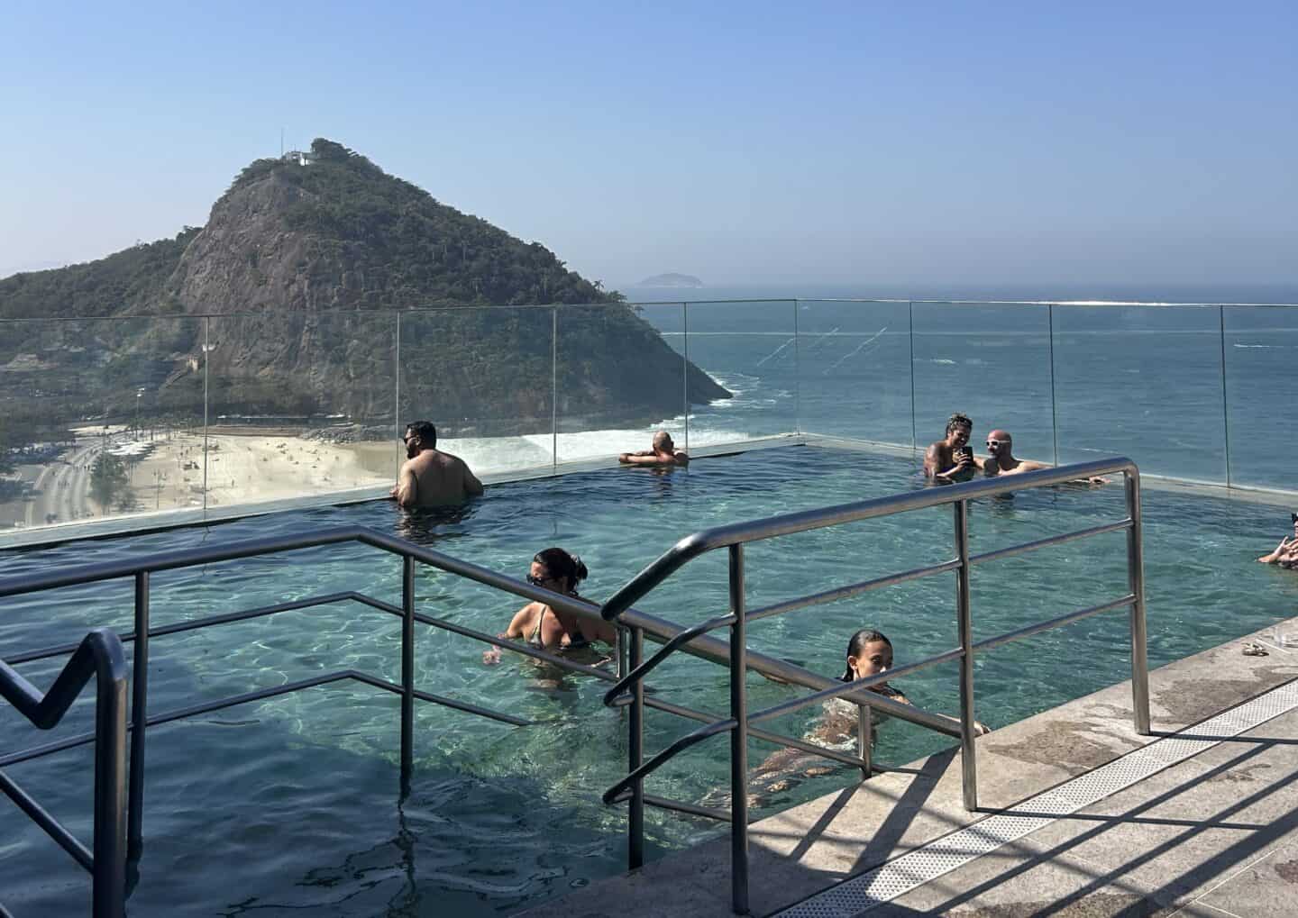 A few people in the rooftop pool overlooking the beach and mountain of Leme at Windsor Leme Hotel, Rio de Janeiro.