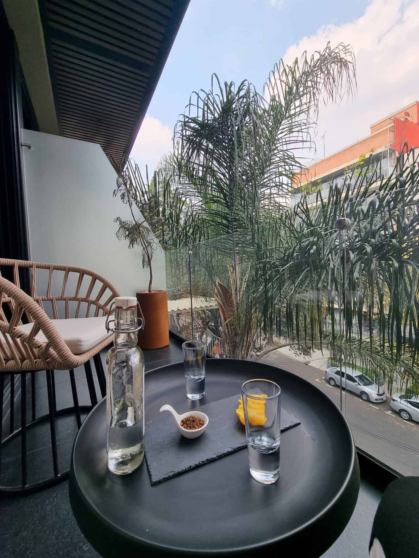 A balcony with plants, a chair, and a table with glasses of water at Condesa Cibel in Mexico City.