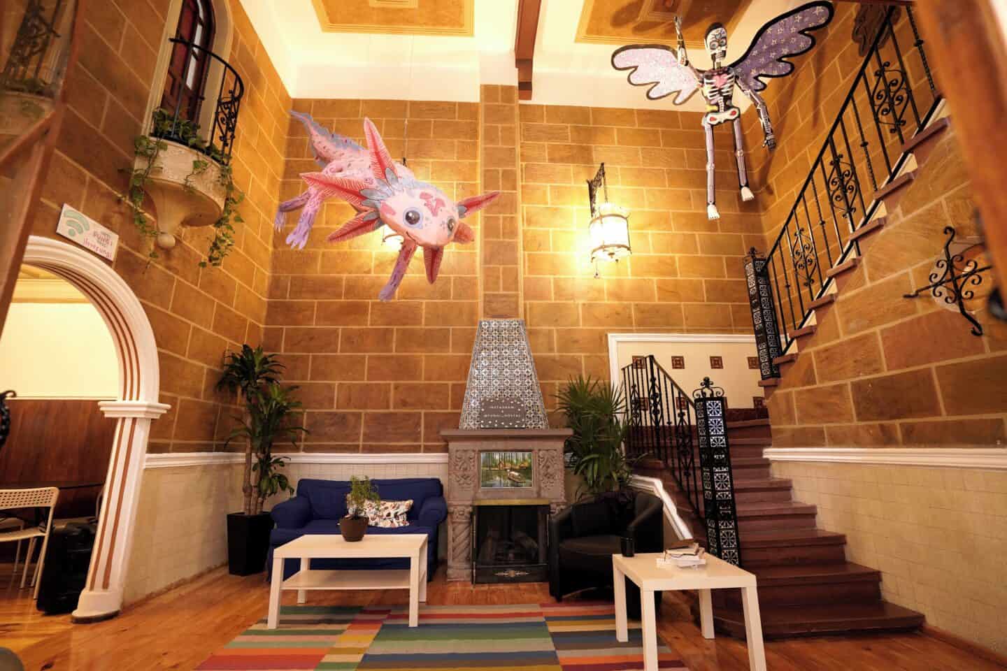 Interior of Hostal Fungi Casa Rosa in Mexico City. A staircase is going up, there's a balcony, seating, and fun decor.