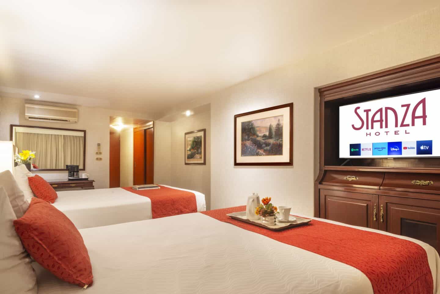 Bedroom with two beds, television that says "Stanza Hotel" and mirror at Hotel Stanza in Mexico City.