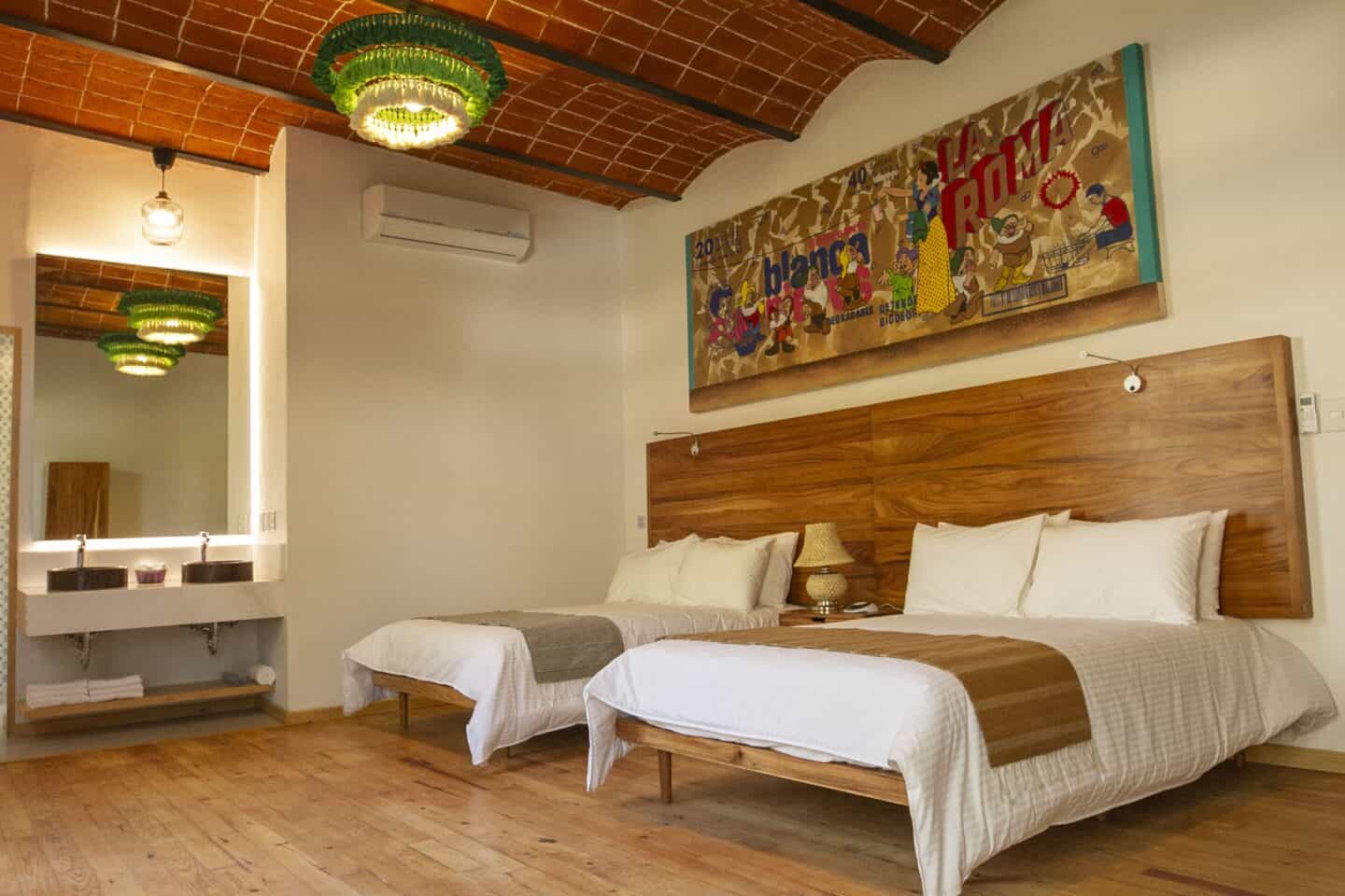 Bedroom with two beds, a wooden headboard, two sinks, and art on the wall at NaNa Vida CDMX.