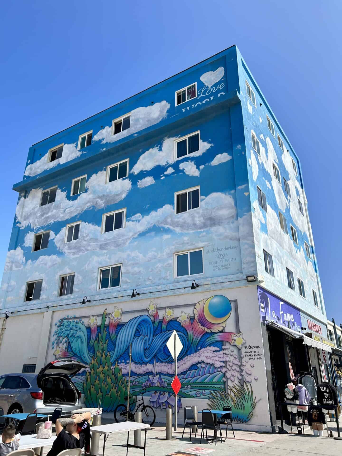 building on Venice Boardwalk in Los Angeles with clouds painted on it and other decorative art.