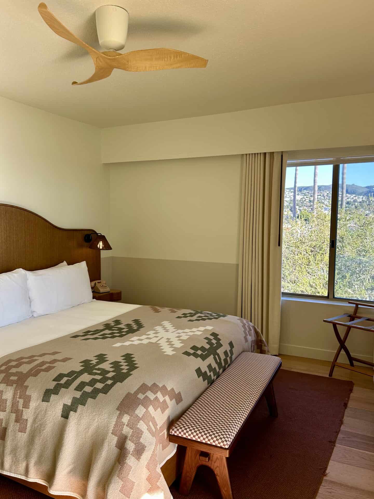 A bed with a fan, and a window inside Casa Loma Beach Hotel in Laguna Beach.