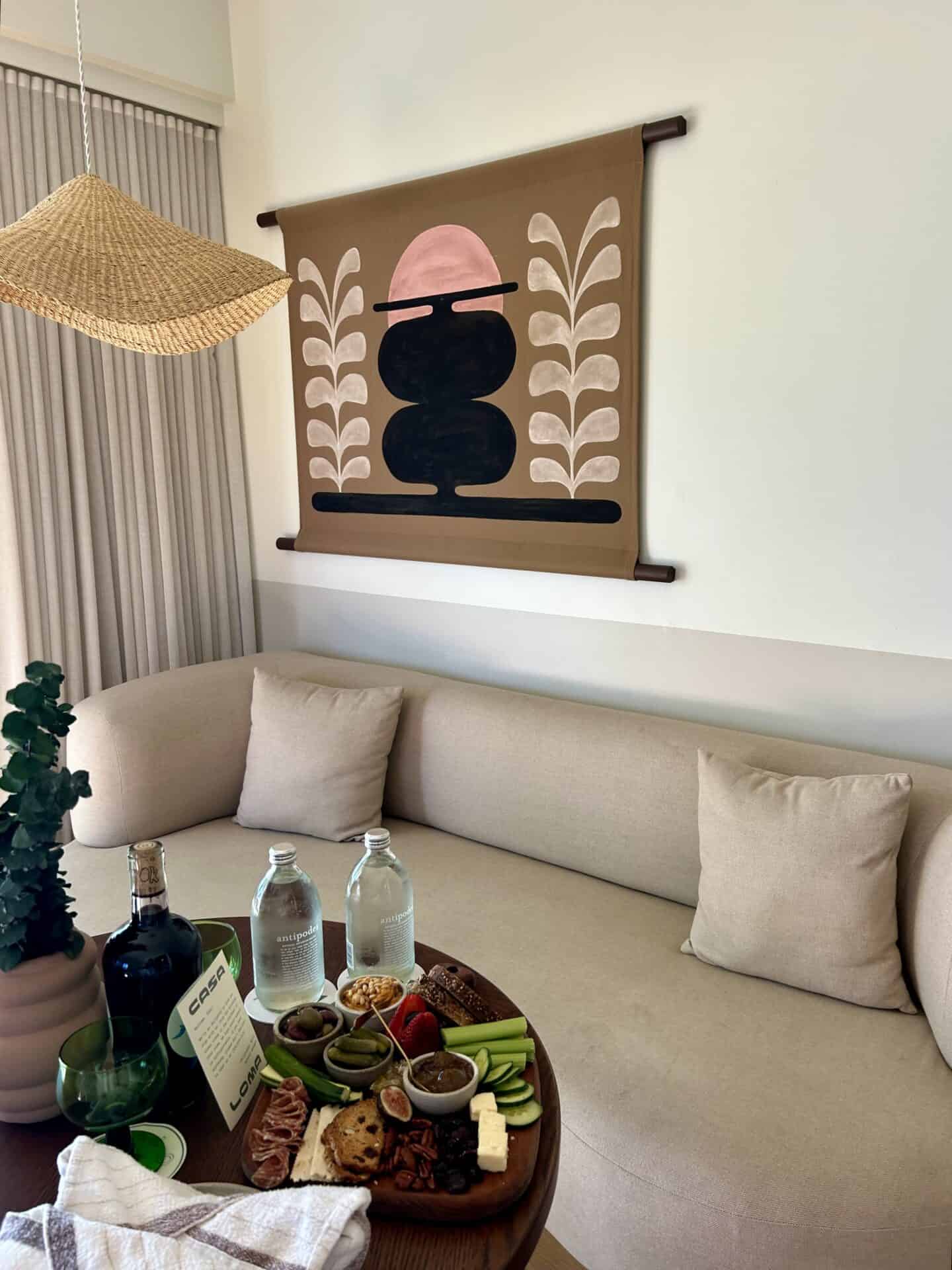 A charcuterie board with two water bottles and a wine bottle on a table in a bedroom at Casa Loma Beach Hotel in Laguna Beach. A couch is behind the table, with a print on the wall.