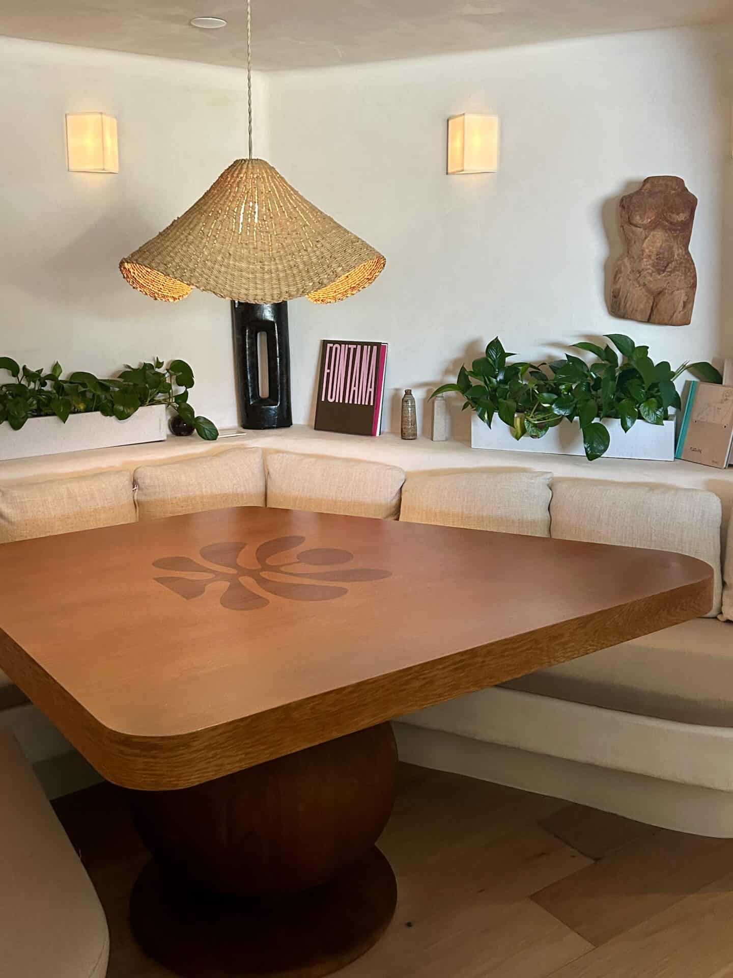 A wooden table with a boho-style lamp, with plants and decor surrounding the table at Casa Loma Beach Hotel in Laguna Beach.