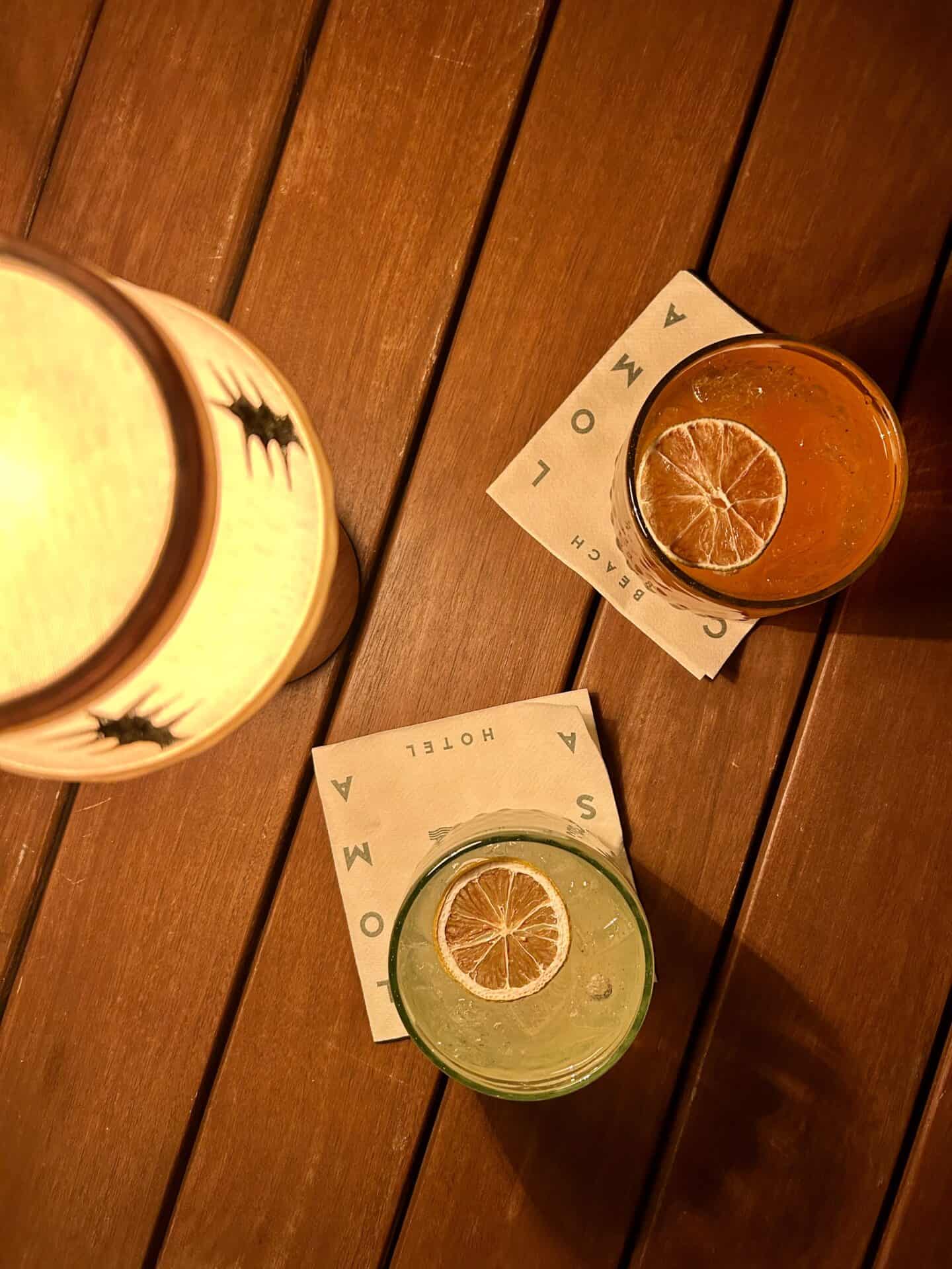 An overhead view of an orange and a yellow cocktail, each with a dried fruit inside, next to a small lamp, at Casa Loma Beach Hotel in Laguna Beach.