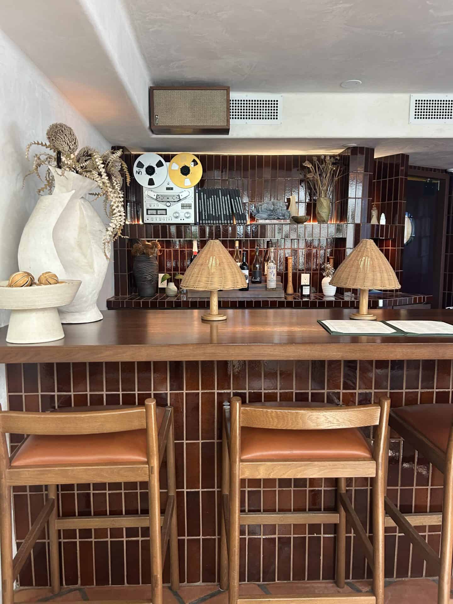 A red-tiled bar with bar seats at Casa Loma Beach Hotel in Laguna Beach. There are wicker lamps, and a menu is open on the bar.