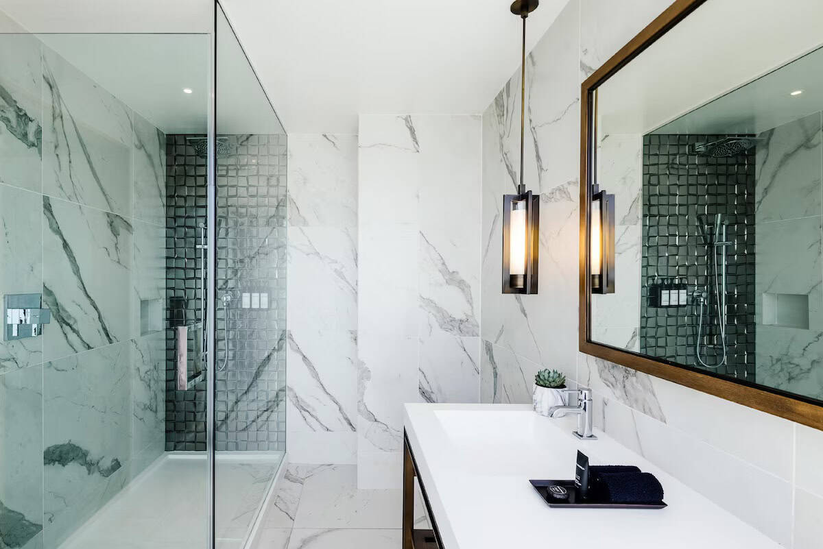 Elegant modern bathroom with marble walls, glass shower, and stylish lighting fixtures.