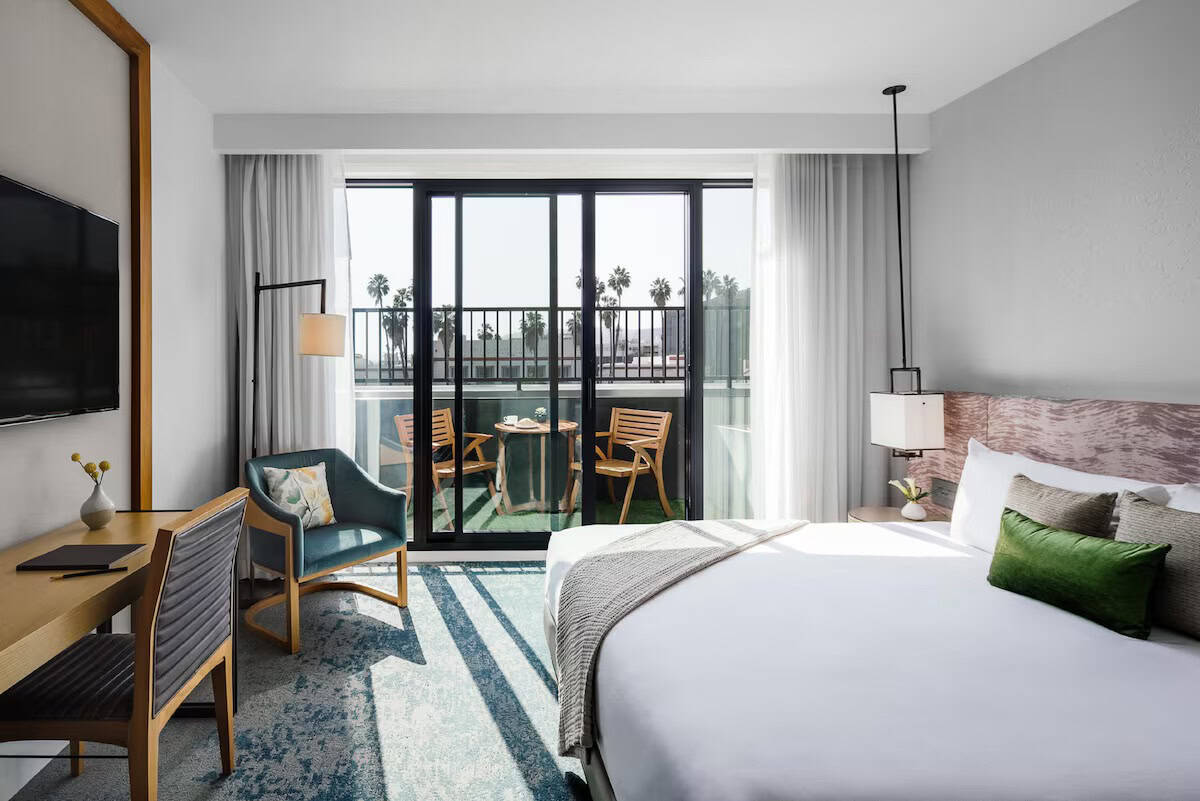 Bright hotel room with balcony, overlooking palm trees and cityscape.