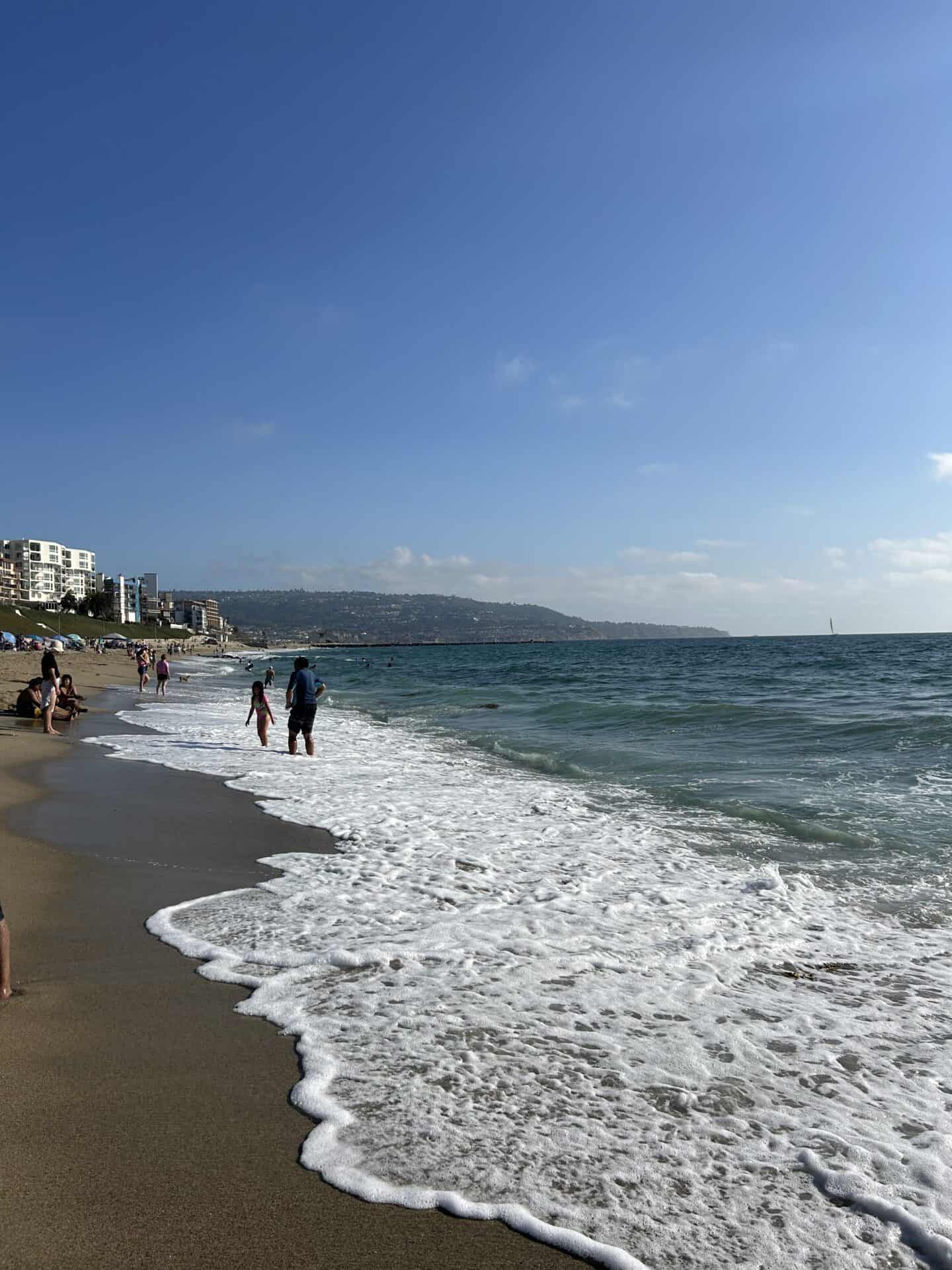 A few people in the ocean in Redondo Beach, California, with mountains visible in the background.